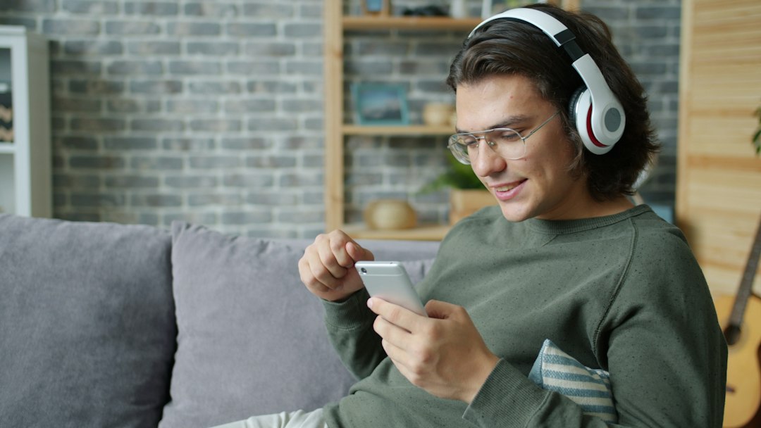 Young man wearing headphones uses smartphone on couch